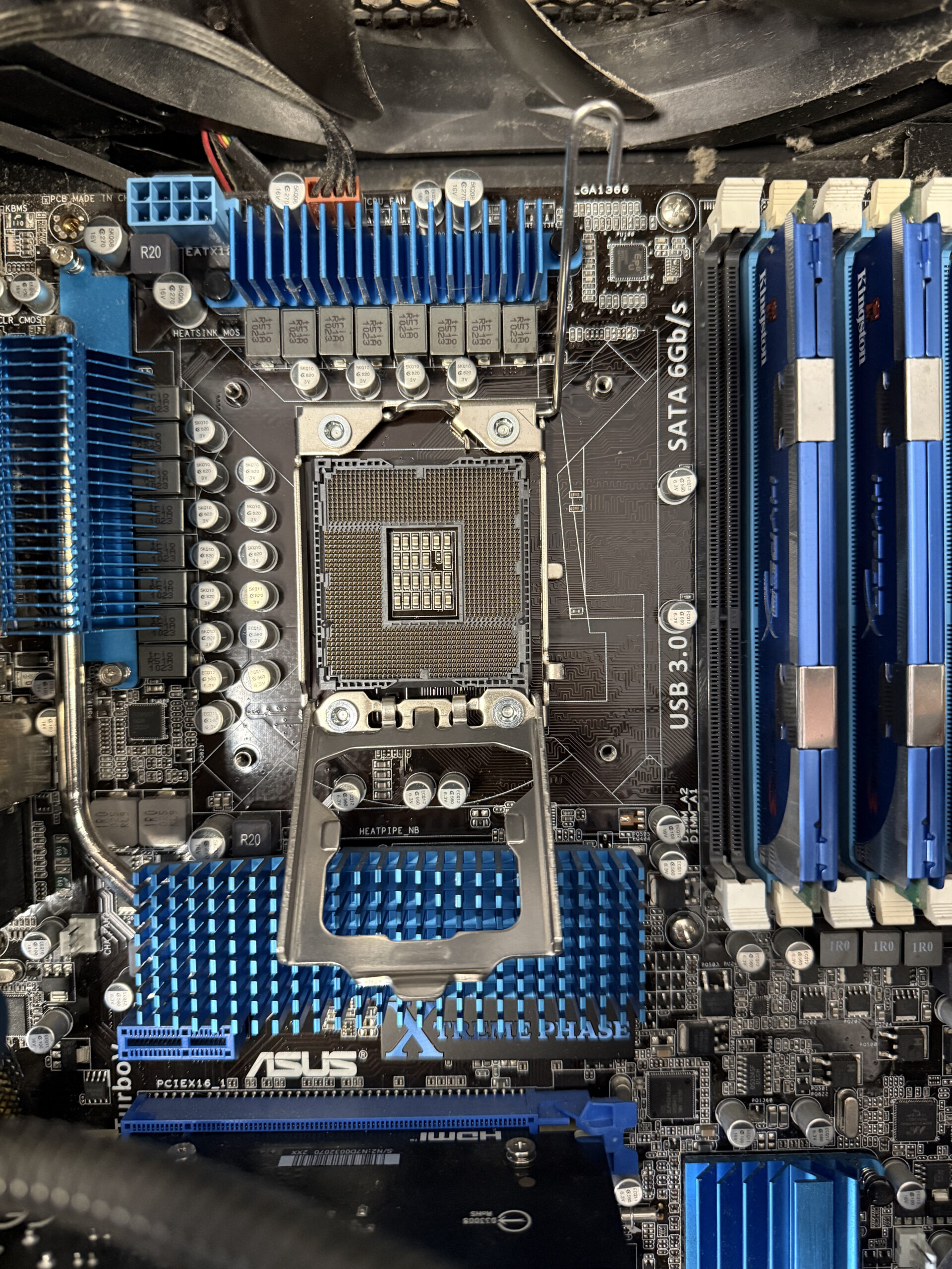 Desktop motherboard with the CPU socket exposed, blue heatsinks and memory modules visible