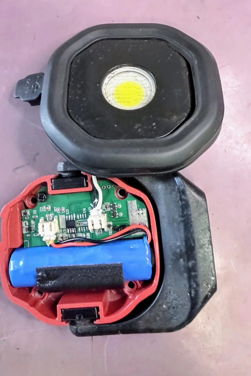 Opened portable LED work light with its battery, wiring and circuit board visible