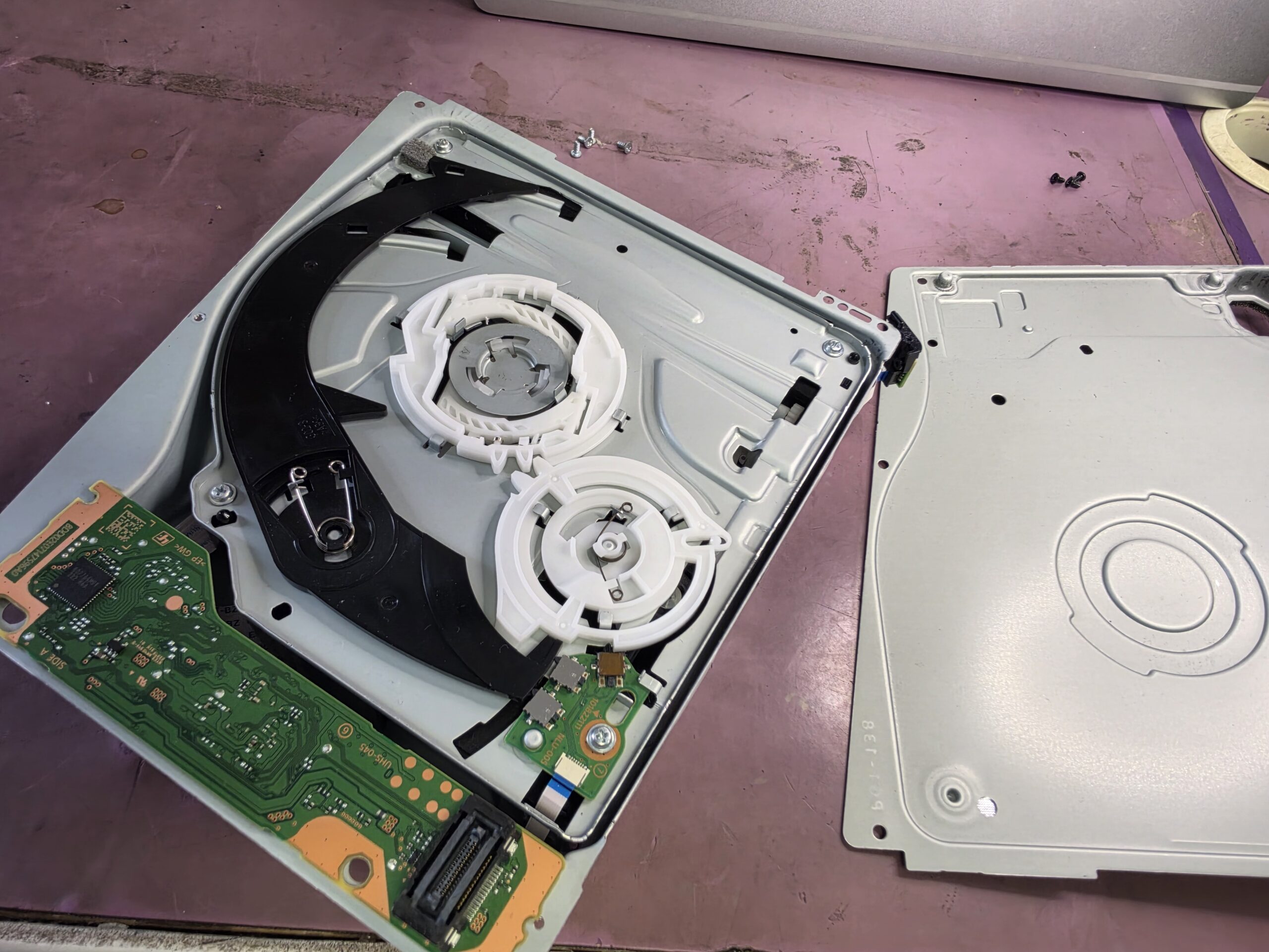 Opened PS5 Slim disc drive showing the internal loading mechanism and removed metal cover