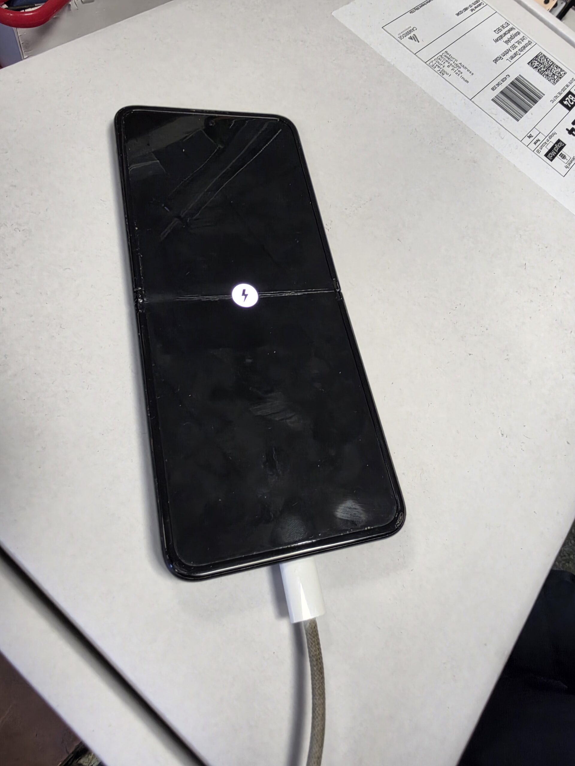 Samsung Galaxy Flip connected to a USB-C cable with a charging symbol visible on the inner display