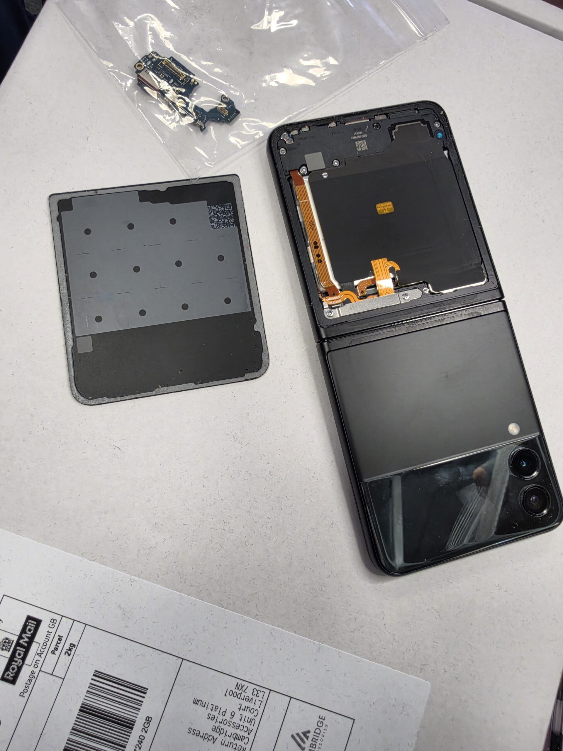Samsung Galaxy Flip opened from the rear, showing internal covers and ribbon connections beside the removed panel