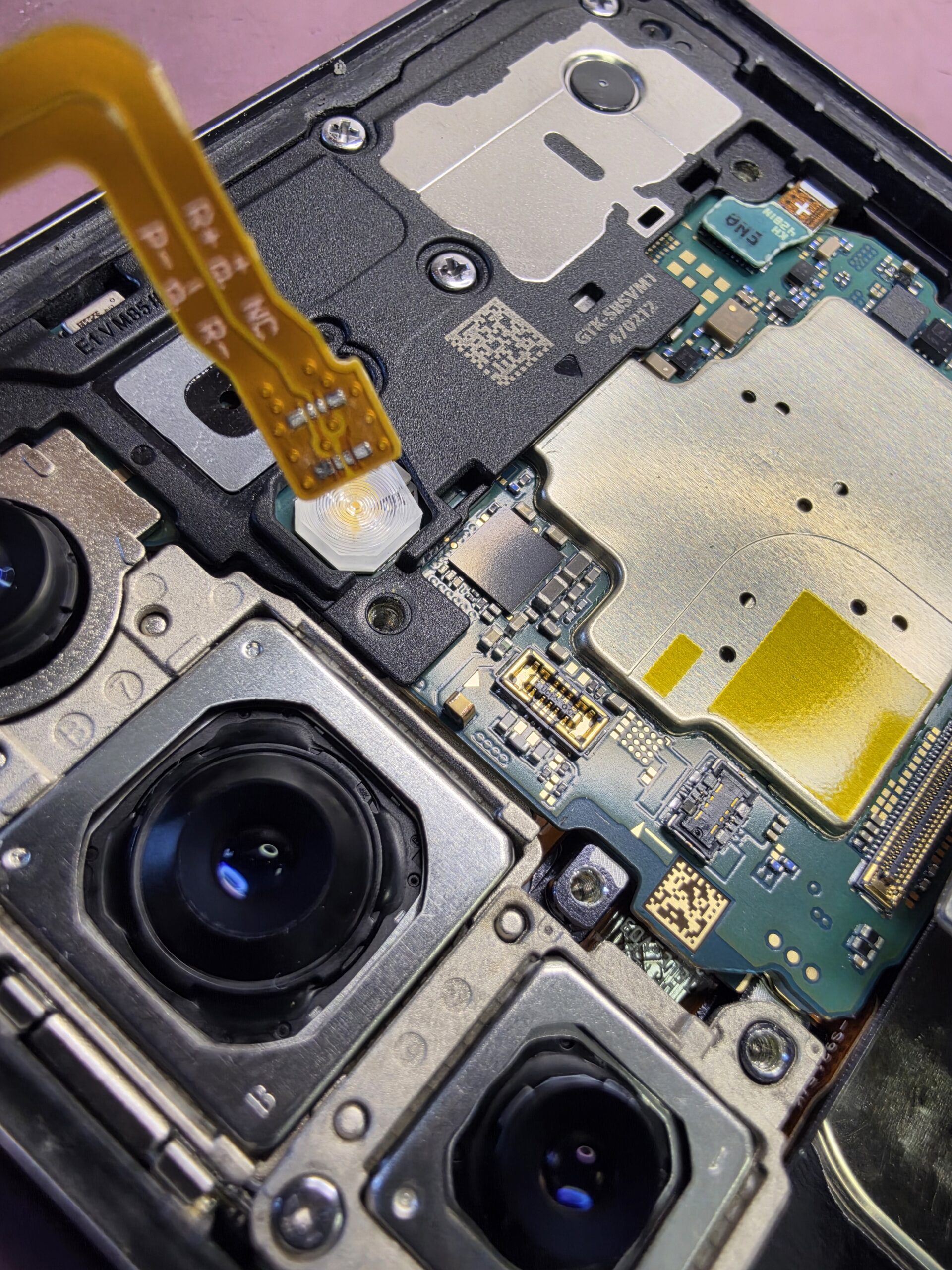 Samsung Galaxy S24 battery flex lifted above the logic board after its battery-side connector detached and remained seated in the board battery socket