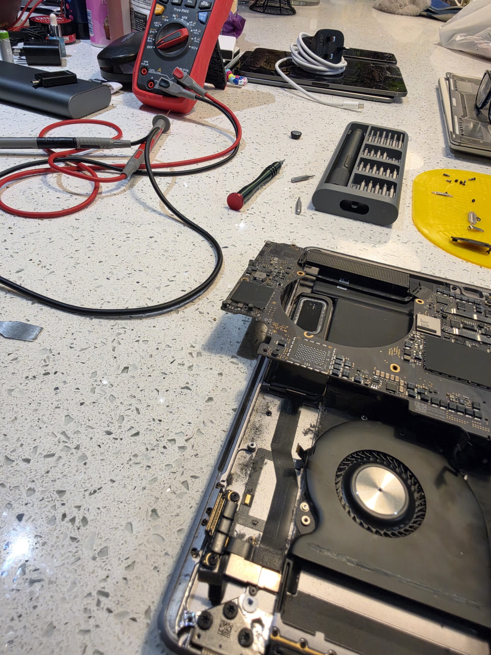 MacBook A1990 logic board lifted from the chassis for board-level diagnosis at iPhoneBits